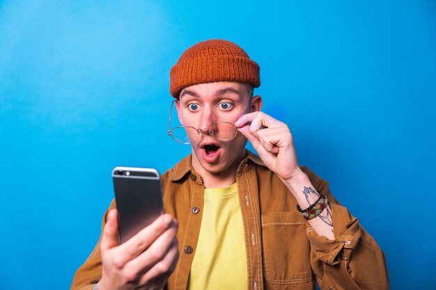 Joven feliz sorprendido celebrando usando una aplicación de teléfono inteligente con fondo azul