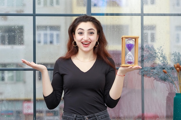 Joven feliz sosteniendo un reloj de arena y mirando a la cámara Foto de alta calidad