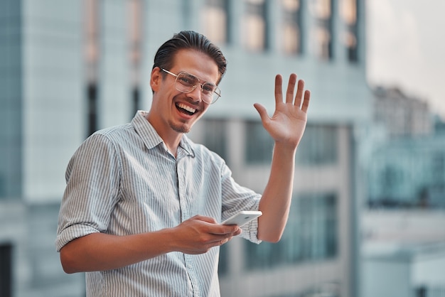 Joven feliz sosteniendo un teléfono en la mano y saludando.