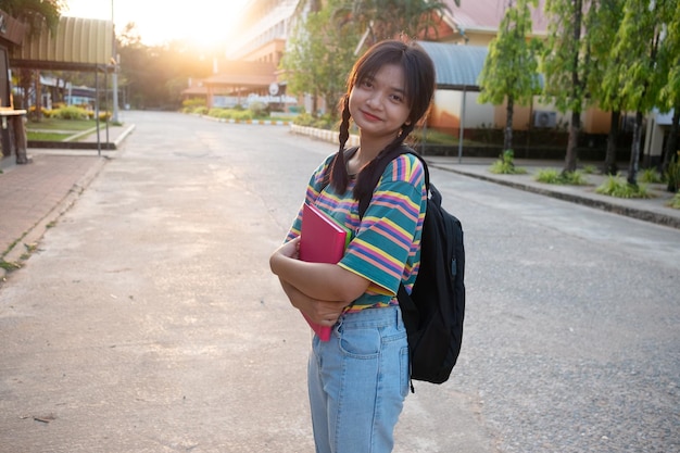 Una joven feliz sostiene un libro con una mochila caminando en la escuela