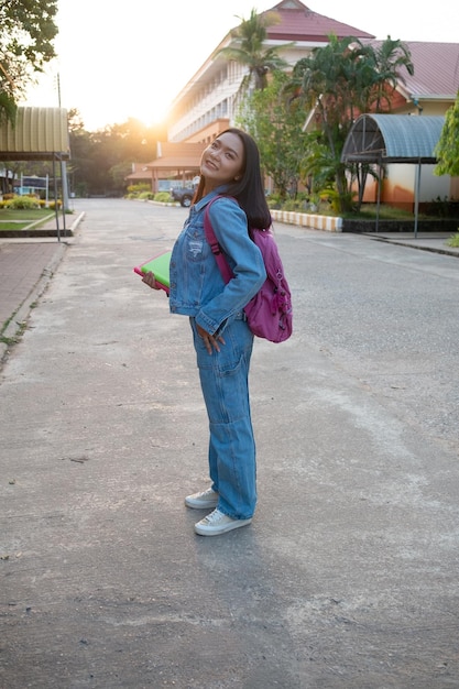 Una joven feliz sostiene un libro con una mochila caminando en la escuela