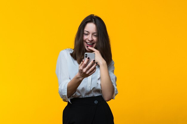 Una joven feliz con un teléfono en las manos con un fondo amarillo