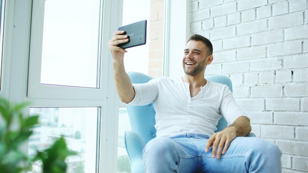 Joven feliz tiene video chat en línea usando una tableta digital sentada en el balcón