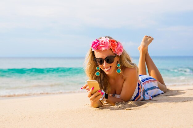 Una joven feliz tumbada en la playa en la arena y usando un teléfono móvil