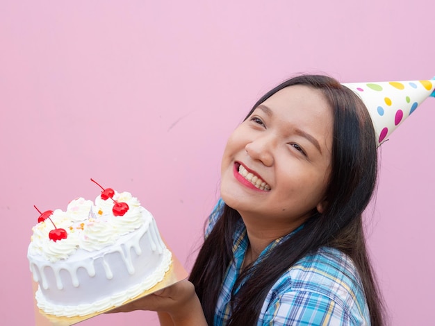 Foto una joven feliz usa un sombrero de fiesta sostiene una tarta con un fondo rosa