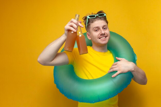 Un joven feliz en el verano de vacaciones sostiene botellas de cerveza y sonríe en un fondo amarillo