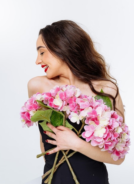 Una joven felizmente sostiene flores rosadas vibrantes en el interior Una joven con cabello largo abraza con alegría un ramo de flores rosadas