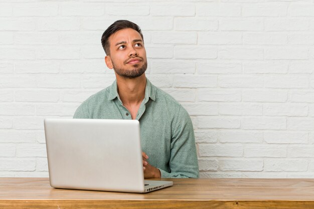 Joven filipino hombre sentado trabajando con su computadora portátil haciendo un plan en mente, creando una idea.