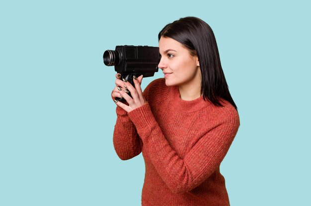 Una joven filma felizmente con una cámara de video antigua en un fondo aislado