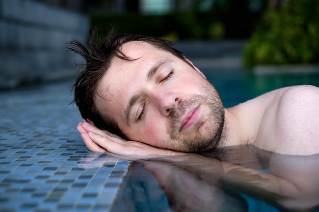 Un joven finge que está durmiendo al borde de la piscina poniendo sus manos debajo de su cabeza