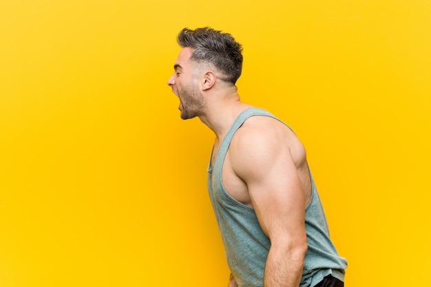 Joven fitness hombre contra amarillo gritando hacia un