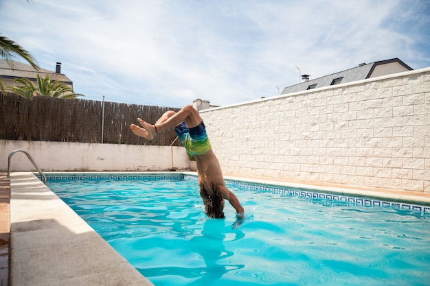 Joven fitness hombre saltando al agua en la piscina un día de vacaciones de verano