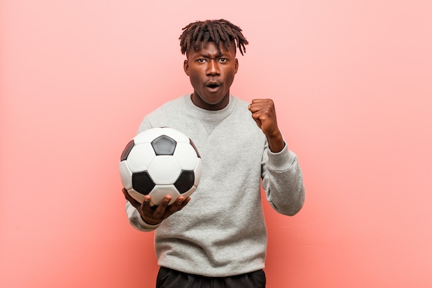 Joven fitness hombre sosteniendo un balón de fútbol animando despreocupado y emocionado