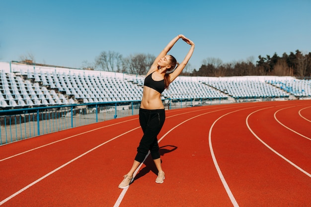 Joven fitness mujer corredor calentar antes de correr en la pista. Ejercicios matutinos en verano