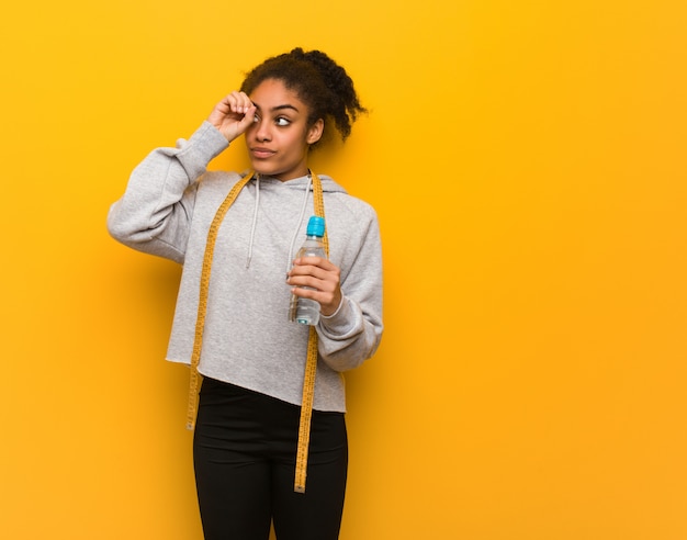 Joven fitness mujer negra haciendo el gesto de un catalejo. Sosteniendo una botella de agua.