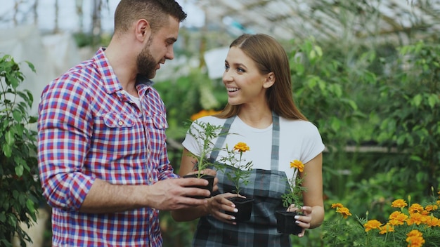 Joven florista amigable hablando con el cliente y dándole consejos mientras trabaja en el jardín