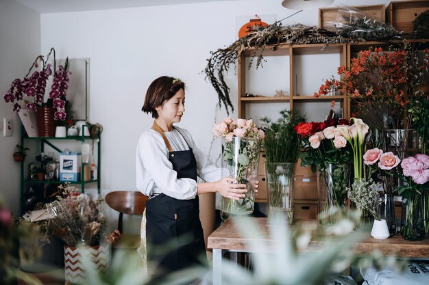 Foto joven florista asiática propietaria de una pequeña tienda de flores que maneja y cuida de flores y plantas frescas en el lugar de trabajo disfrutando de su trabajo para estar con las flores concepto de pequeña empresa