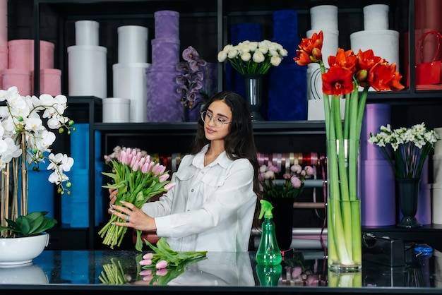 Una joven florista cuida las flores en una floristería acogedora y recoge ramos de flores Floristería y fabricación de baldes en una floristería Pequeña empresa