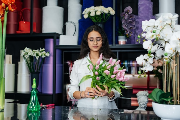 Una joven florista cuida las flores en una floristería acogedora y recoge ramos de flores Floristería y fabricación de baldes en una floristería Pequeña empresa