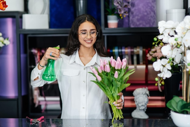 Una joven florista cuida las flores en una floristería acogedora y recoge ramos de flores Floristería y fabricación de baldes en una floristería Pequeña empresa