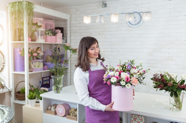 Joven florista feliz haciendo arreglos de flores frescas en caja de regalo