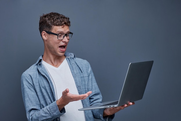 Joven en un fondo gris sosteniendo una computadora portátil