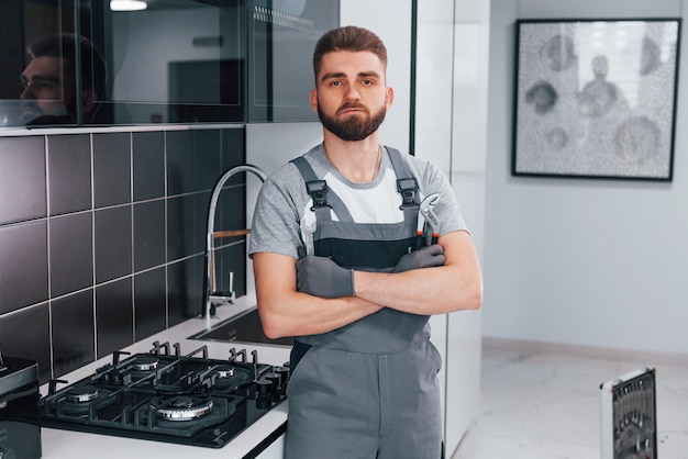 Joven fontanero profesional con uniforme gris parado en la cocina