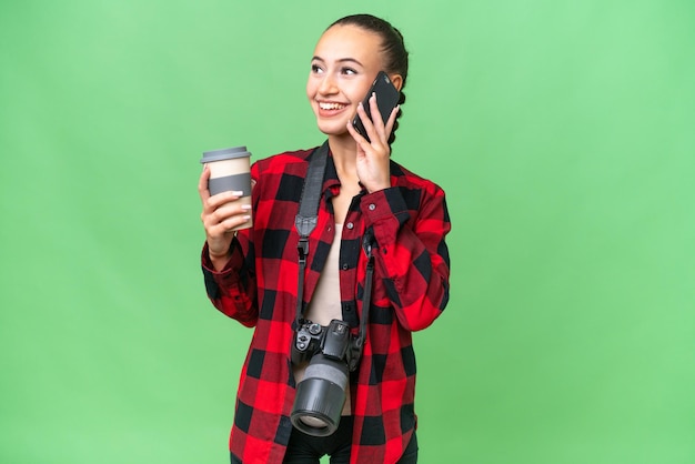 Joven fotógrafa árabe sobre un fondo aislado sosteniendo café para llevar y un móvil