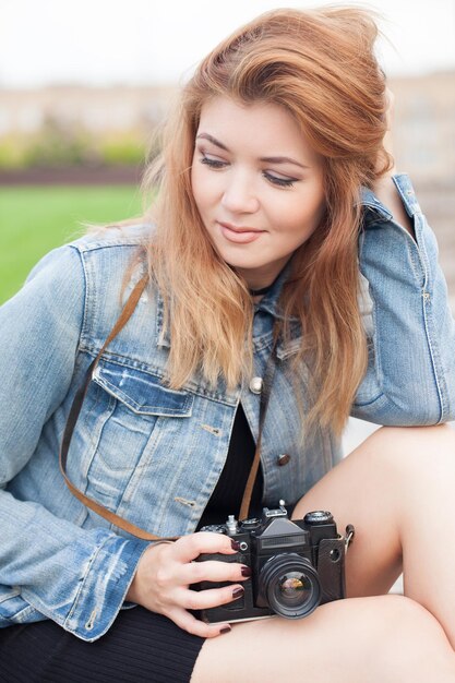 Joven fotógrafa caminando por la calle con una chaqueta de jeans con una cámara vieja