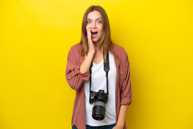 Joven fotógrafa caucásica aislada de fondo amarillo con sorpresa y expresión facial conmocionada