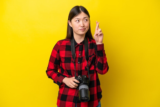 Joven fotógrafa china aislada de fondo amarillo con los dedos cruzados y deseando lo mejor
