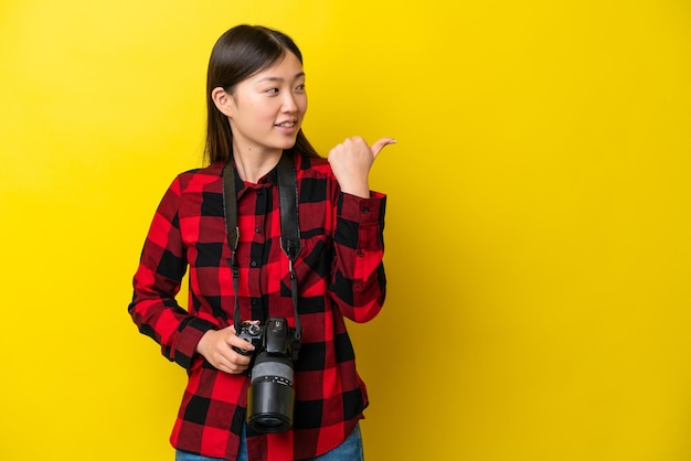 Joven fotógrafa mujer china aislada de fondo amarillo apuntando hacia un lado para presentar un producto