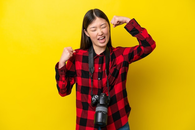 Joven fotógrafa mujer china aislada de fondo amarillo celebrando una victoria