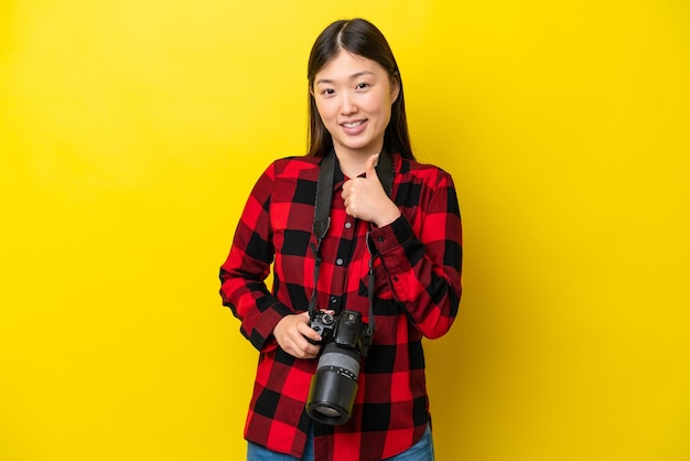 Joven fotógrafa mujer china aislada de fondo amarillo dando un gesto de pulgar hacia arriba