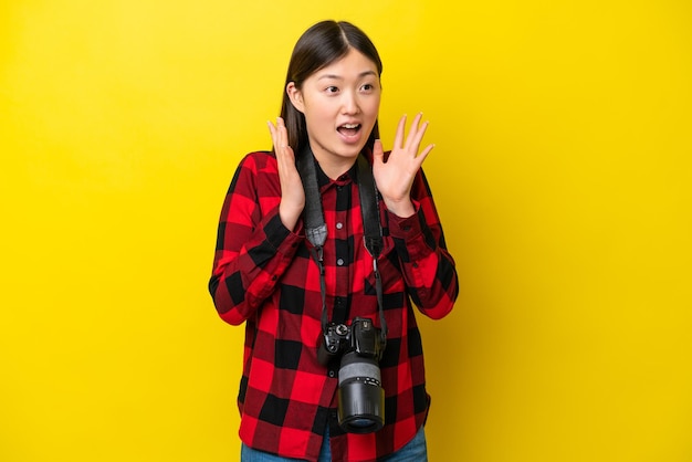 Joven fotógrafa mujer china aislada de fondo amarillo con expresión facial sorpresa