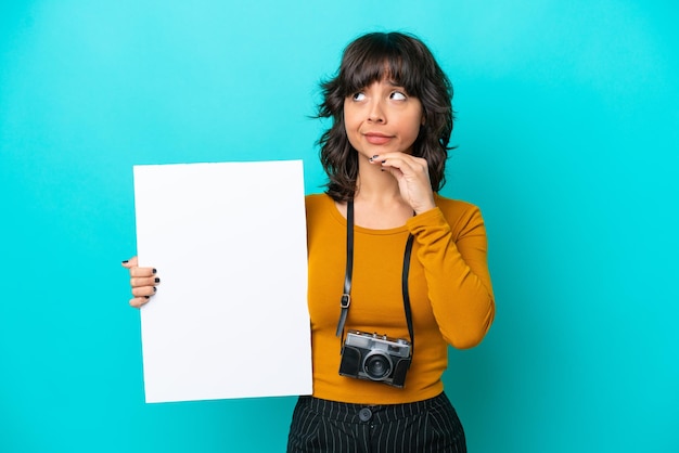 Joven fotógrafa mujer latina aislada de fondo azul sosteniendo un cartel vacío y pensando