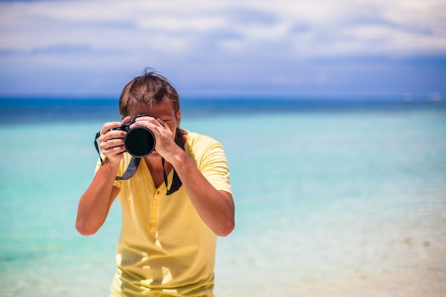 Joven fotografiando con la cámara en sus manos en una playa tropical