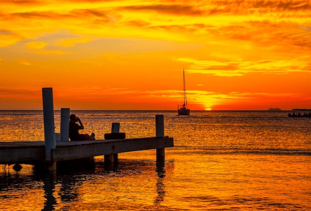 Un joven fotografiando la puesta de sol de Roatán sentado en un muelle de madera en West End