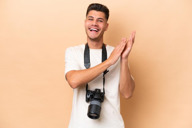 Joven fotógrafo caucásico aislado de fondo beige aplaudiendo después de la presentación en una conferencia