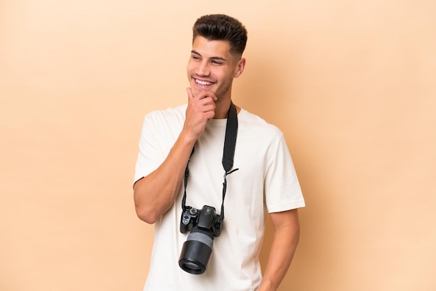 Joven fotógrafo hombre caucásico aislado de fondo beige mirando hacia un lado