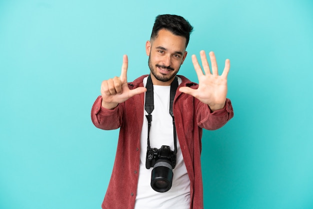 Joven fotógrafo hombre caucásico aislado sobre fondo azul contando siete con los dedos