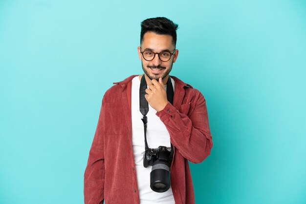 Joven fotógrafo hombre caucásico aislado sobre fondo azul con gafas y sonriendo