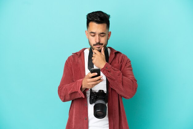 Joven fotógrafo hombre caucásico aislado sobre fondo azul pensando y enviando un mensaje