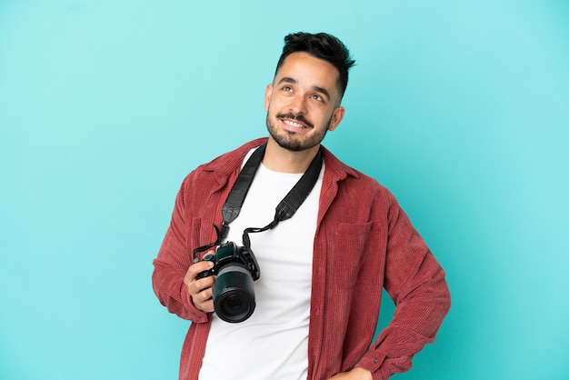 Joven fotógrafo hombre caucásico aislado sobre fondo azul posando con los brazos en la cadera y sonriendo