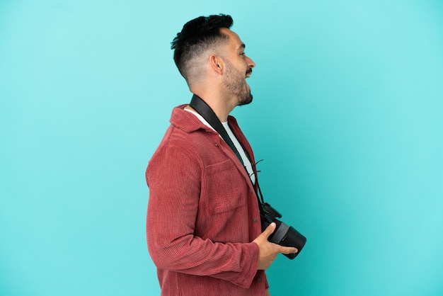 Joven fotógrafo hombre caucásico aislado sobre fondo azul riendo en posición lateral