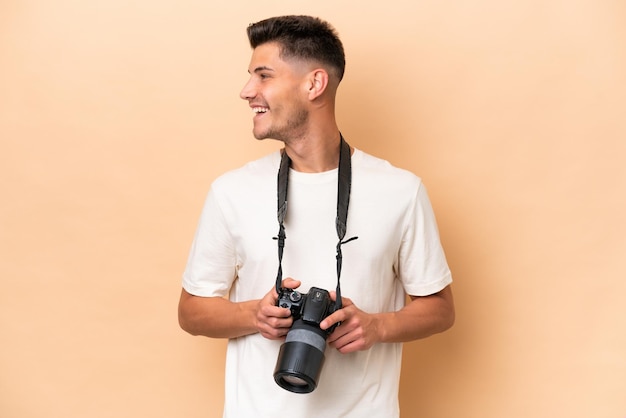 Joven fotógrafo hombre caucásico aislado sobre fondo beige mirando hacia el lado