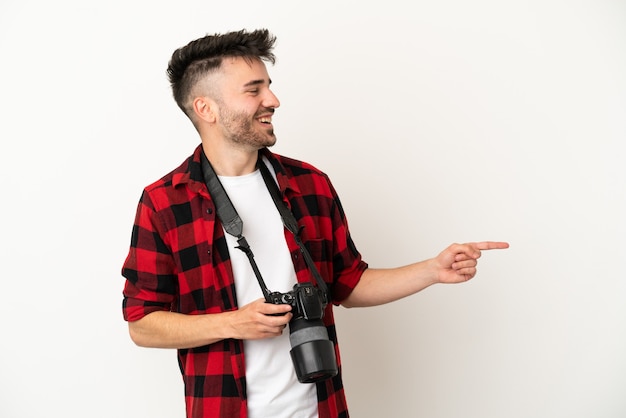 Joven fotógrafo hombre caucásico aislado sobre fondo blanco apuntando con el dedo hacia un lado y presentando un producto