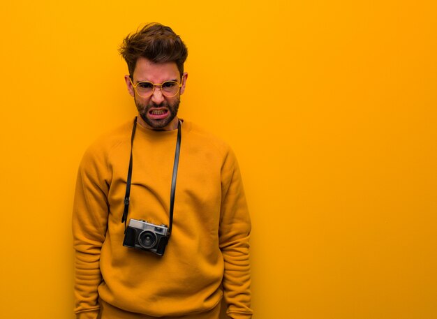 Joven fotógrafo hombre gritando muy enojado y agresivo