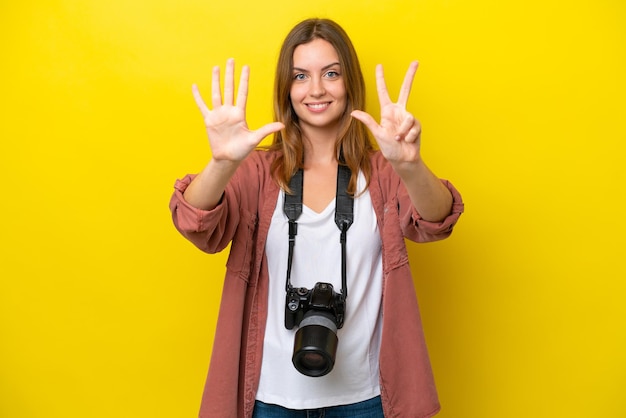Joven fotógrafo mujer caucásica aislada sobre fondo amarillo contando ocho con los dedos