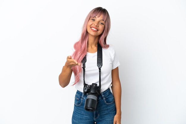Foto joven fotógrafo mujer de raza mixta con cabello rosado aislado sobre fondo blanco un apretón de manos para cerrar un buen trato